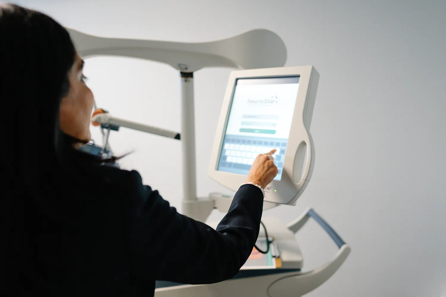 A woman uses a touchscreen interface on a TMS machine in a modern clinical setting, highlighting advanced technology in healthcare environments.
