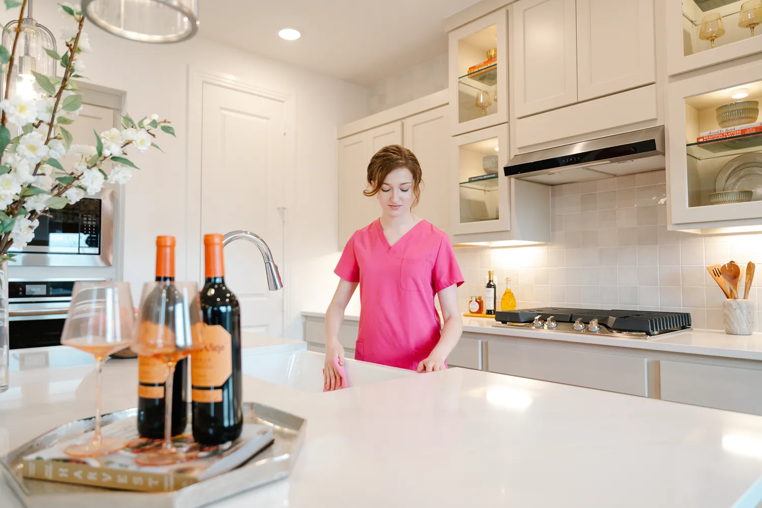 Professional cleaner in pink scrubs wipes down a modern white kitchen sink.