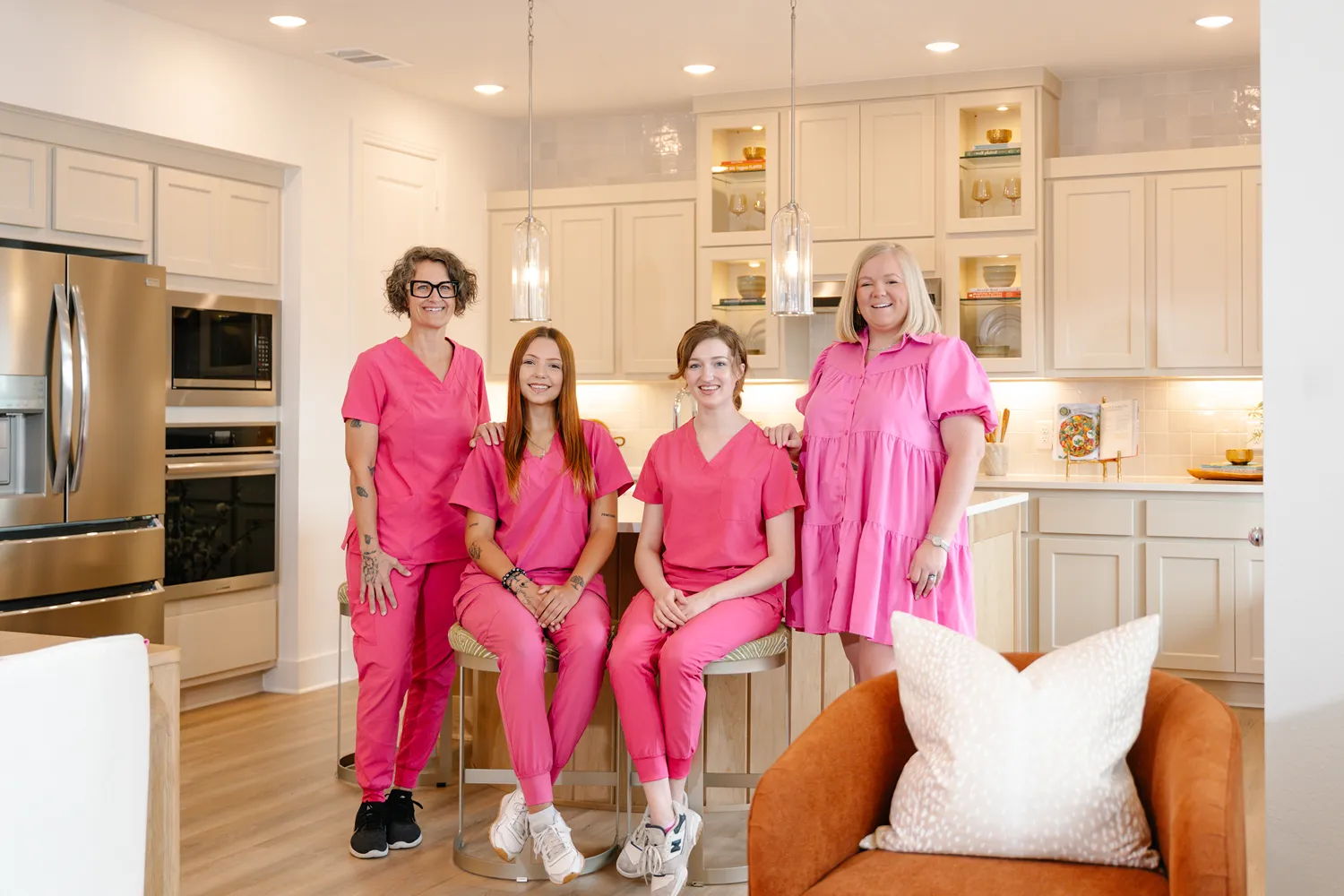 Four women in coordinating pink uniforms pose in a clean, modern kitchen as a professional cleaning team.