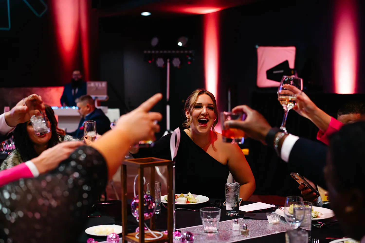 A woman in a black dress laughs as people around her raise glasses for a toast at a StatLab corporate event, with festive pink lighting in the background.