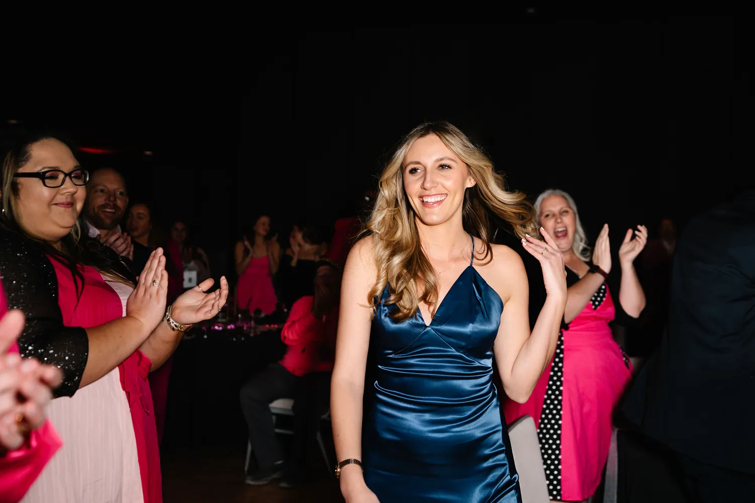 A woman in a blue satin dress smiles while walking through a crowd applauding her at an awards ceremony in Dallas, Texas.