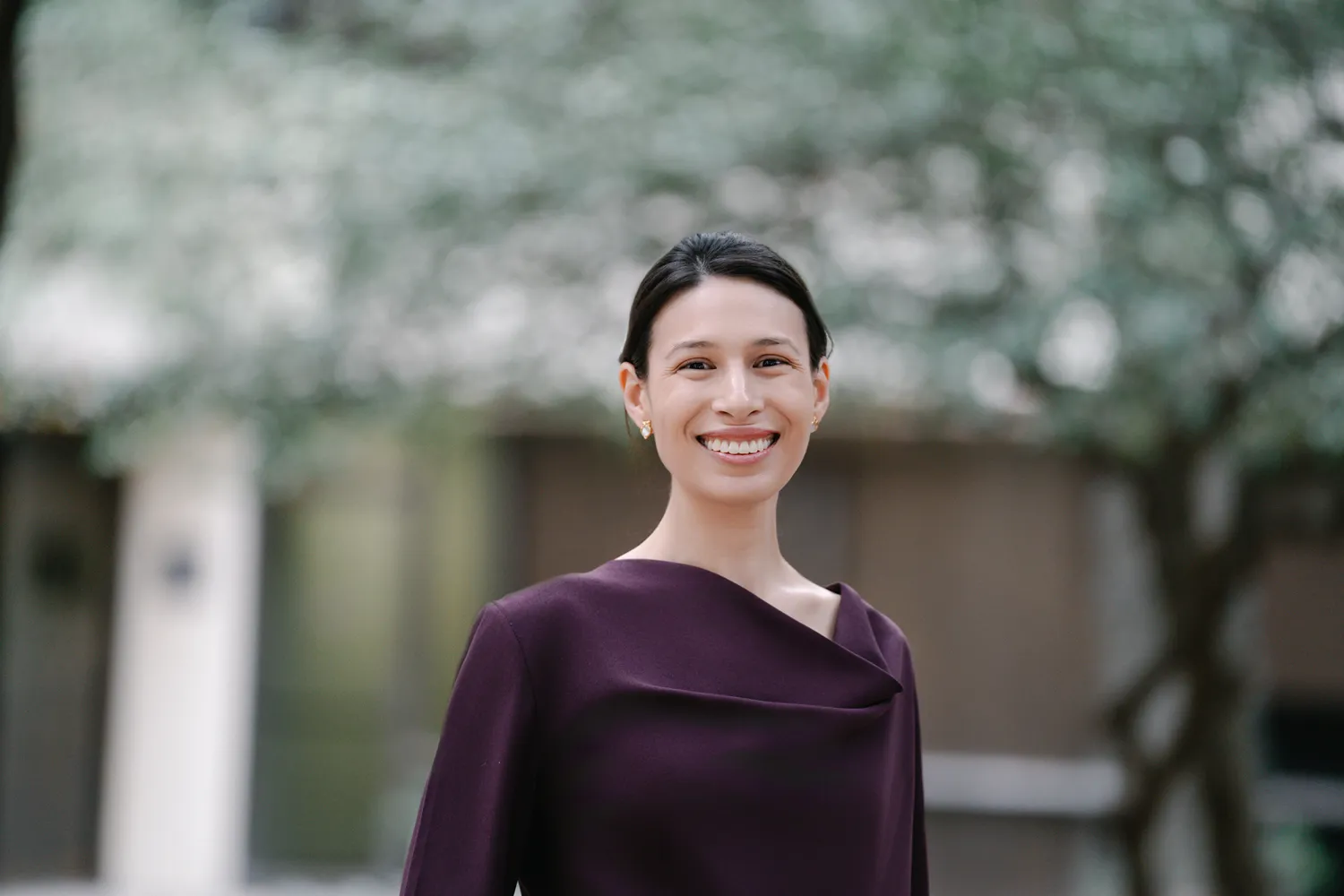 Professional traditional headshot of a woman in a maroon dress, standing outside with a soft-focus background—ideal for LinkedIn profiles, company directories, and corporate uses.